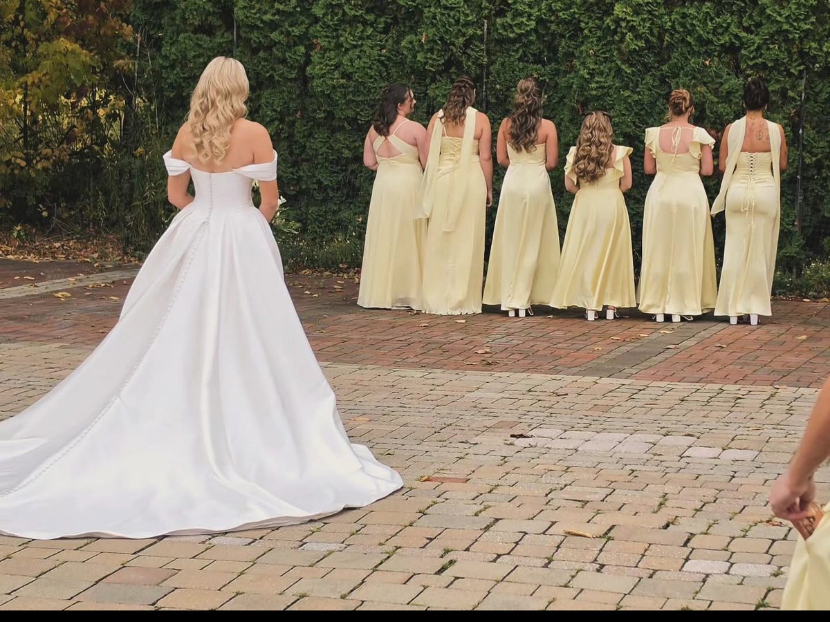 Bride in a white gown facing her bridesmaids in pale yellow dresses